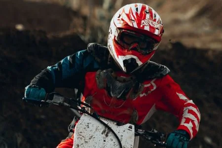 Person with helmet and goggles on riding a dirt bike.