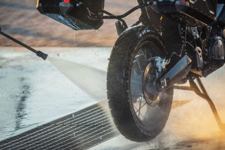 Person rinsing cleaner off motorcycle with a hose.