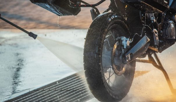Person rinsing cleaner off motorcycle with a hose.